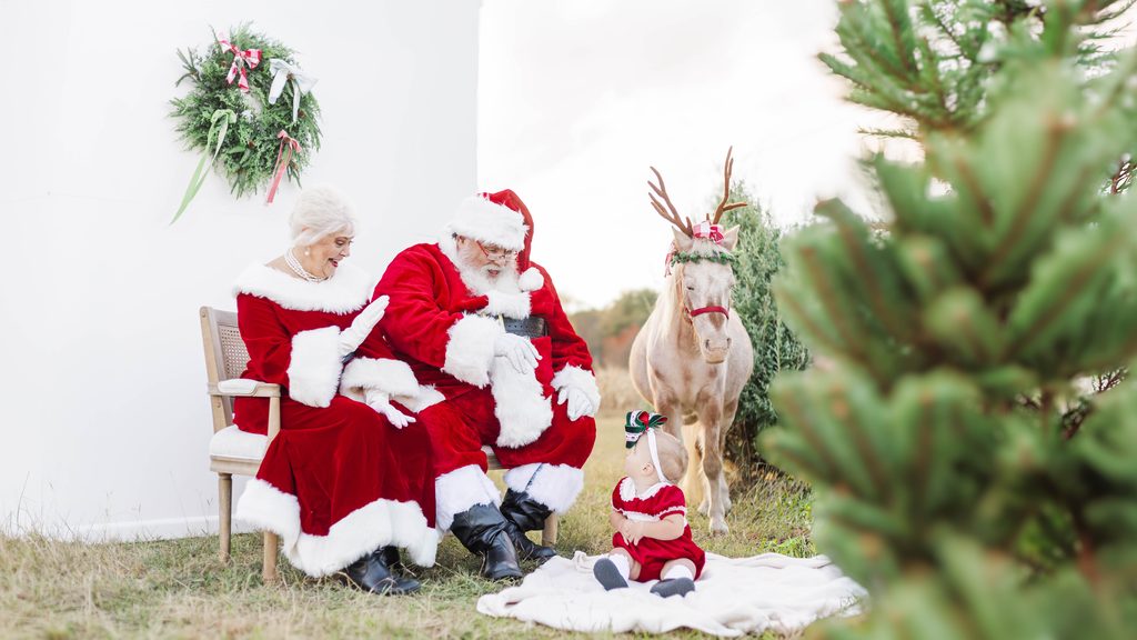 Santa Claus and Mrs. Claus sitting with a baby beside Burt the Reindeer during a Christmas photography session with 5U Photography in Birmingham, Alabama.