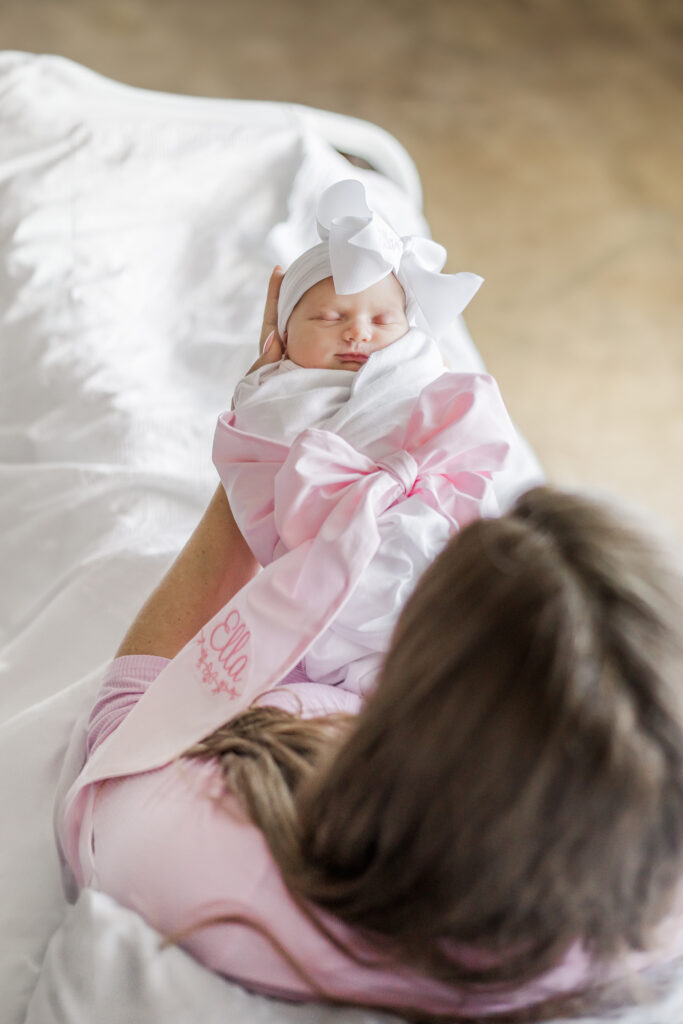 Mom looking down at newborn baby girl wrapped in a white swaddle with pink bow during a fresh- 48 session at Grandview Medical Center in Birmingham AL
