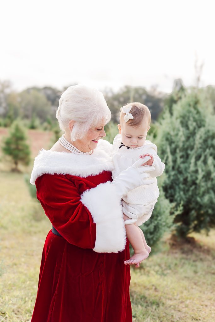 Mrs. Claus holding a baby dressed in white during a magical Christmas mini session with 5U Photography near Birmingham, Alabama.