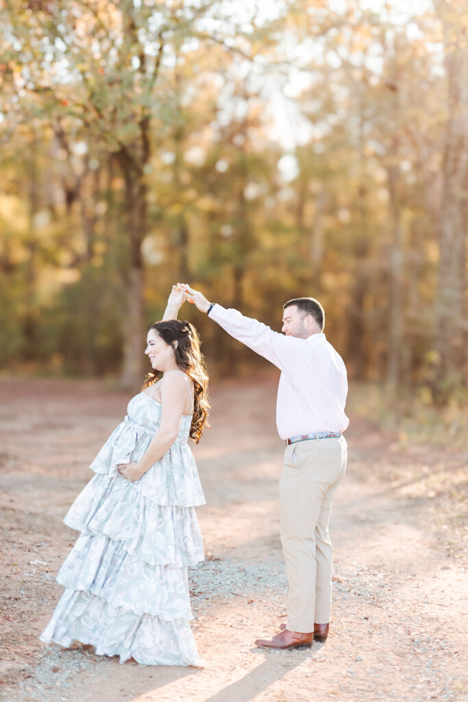 Expecting couple dancing on dirt road in a picturesque fall wooded path during their maternity session at Old Baker Farm in Birmingham, AL