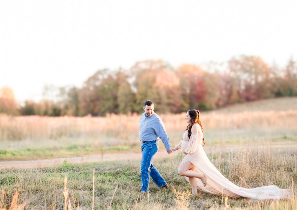 Expecting couple walking hand-in-hand through a picturesque fall field during their maternity session