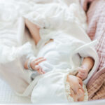 newborn baby girl laying in hospital crib wearing white shirt and bonnet during fresh-48 session 