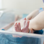 close up of baby boy's feet lying in hospital crib while being swaddled by mother during fresh-48 session