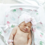 close up of baby girl laying in hospital crib with hat on at Brookwood Hospital 