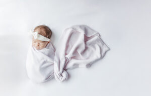 newborn baby girl wrapped in pink swaddle with white bow sleeping peacefully during the newborn session included in the Yonke Family's milestone membership with 5U Photography
