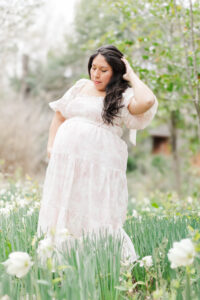 Close-up of expecting mother’s hands on her baby bump, surrounded by blooming tulips in soft spring sunlight during maternity session with 5U Photography