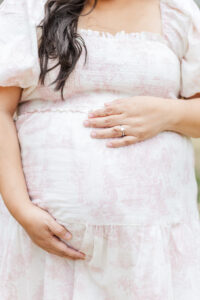Close-up of expecting mother’s hands on her baby bump, surrounded by blooming tulips in soft spring sunlight
