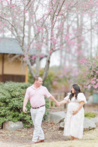 Expecting mom and dad holding hands in front of a backdrop of colorful flowers during spring maternity session at the botanical gardens