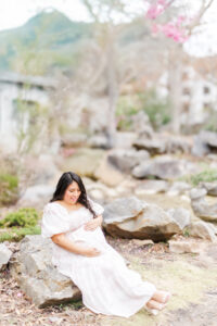 Soft light filtering through cherry blossoms, highlighting the expecting mother as she poses gracefully during spring maternity session with 5U Photography