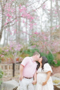 Expecting mom and dad sharing a tender moment, standing together under the canopy of cherry blossoms at Birmingham Botanical Gardens
