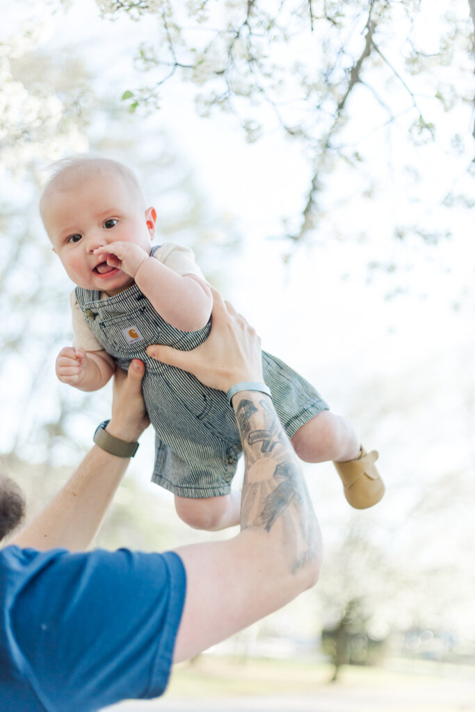 Dad holding 6 month old walker during 6 month spring milestone session at Black creek dog park in fultondale alabama