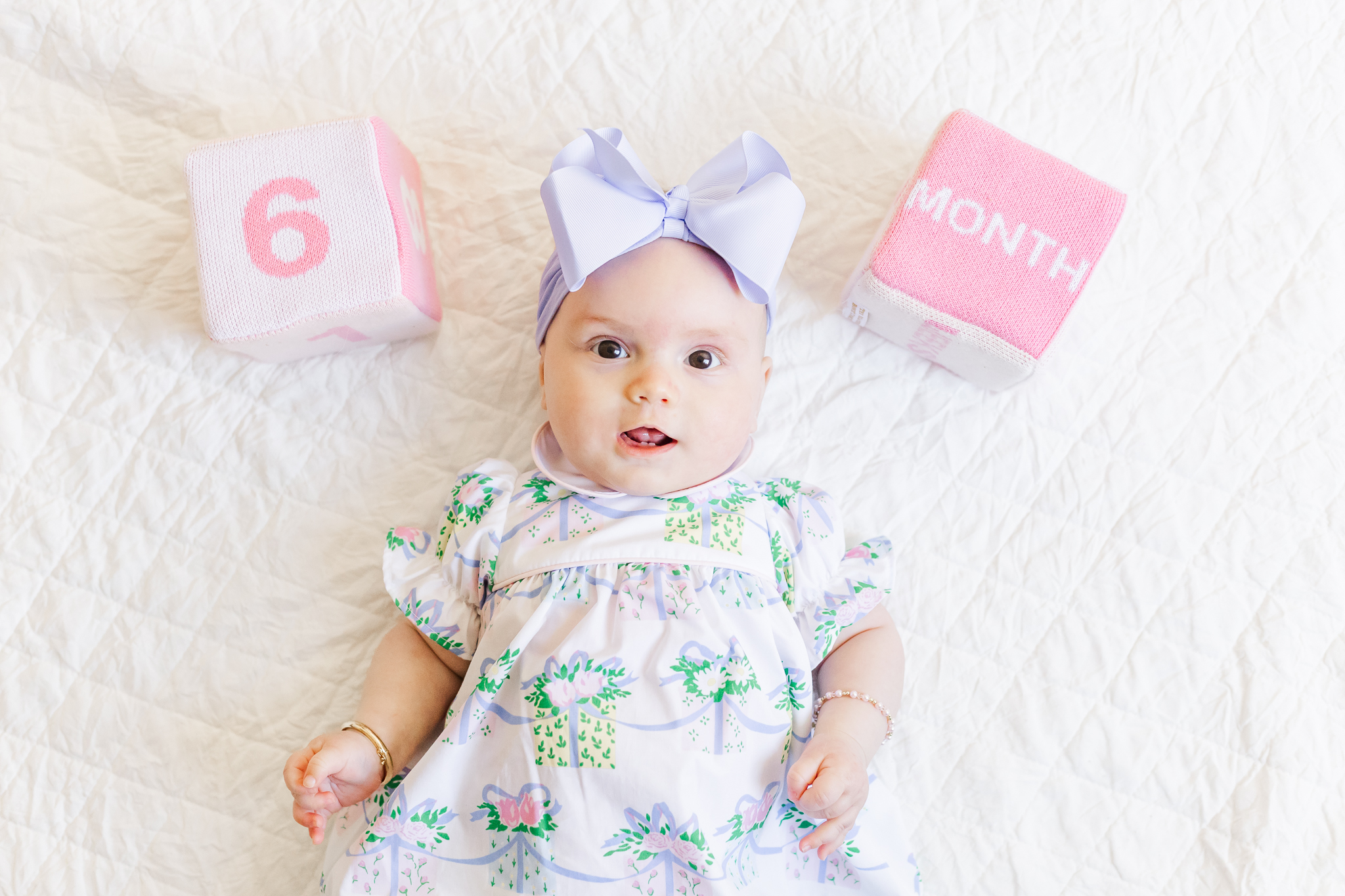 picture of 6 month baby girl with purpule bow laying on blanket with 2 blocks beside her with 6 and months on them during 6 month milestone membership session with 5U Photography