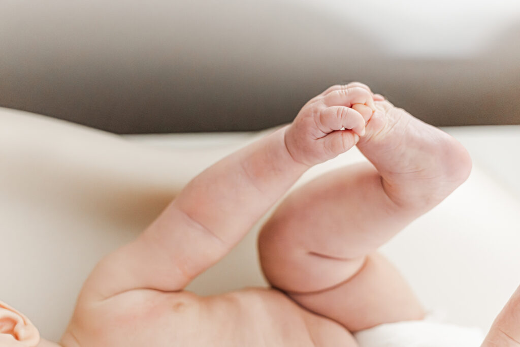 close up of 6 month old little girl holding her foot while laying on changing table during milestone session with 5U Photography