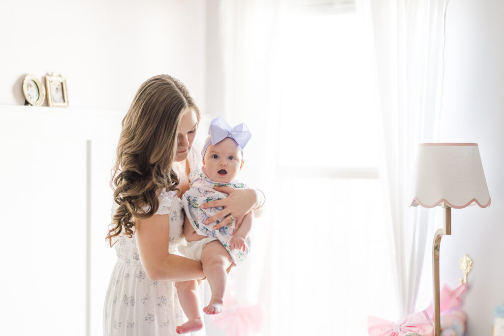Baby Ella grinning with happiness as mom holds her up for a sweet photo in their light and airy home