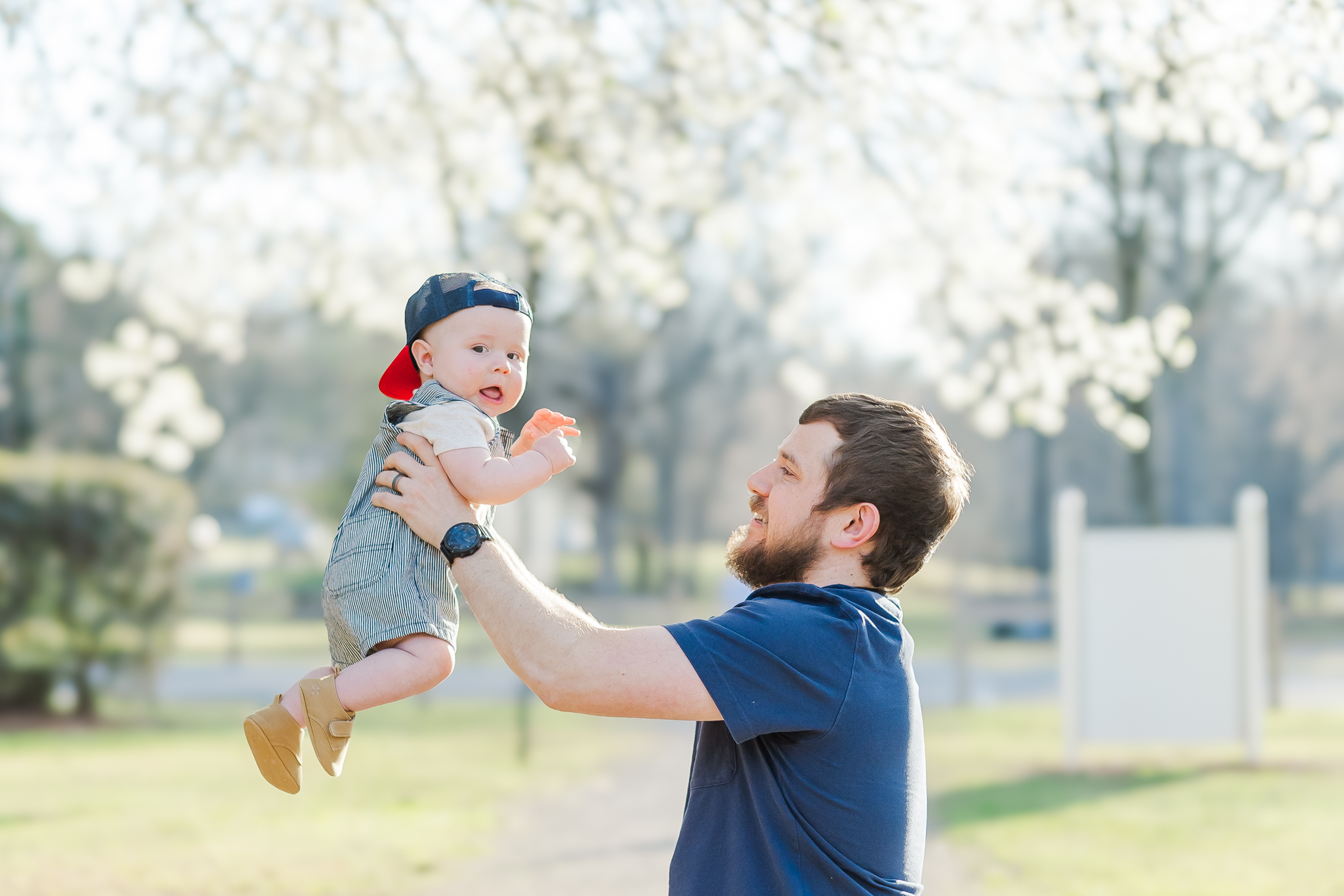Dad standing on path at park holding 6 month old son in the air during 6 month spring milestone session