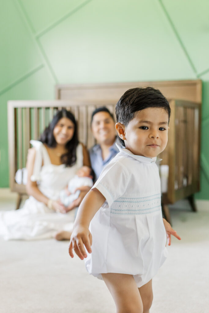 Lifestyle newborn photography in Trussville, Alabama featuring toddler big brother in the foreground with parents and newborn blurred in the background.