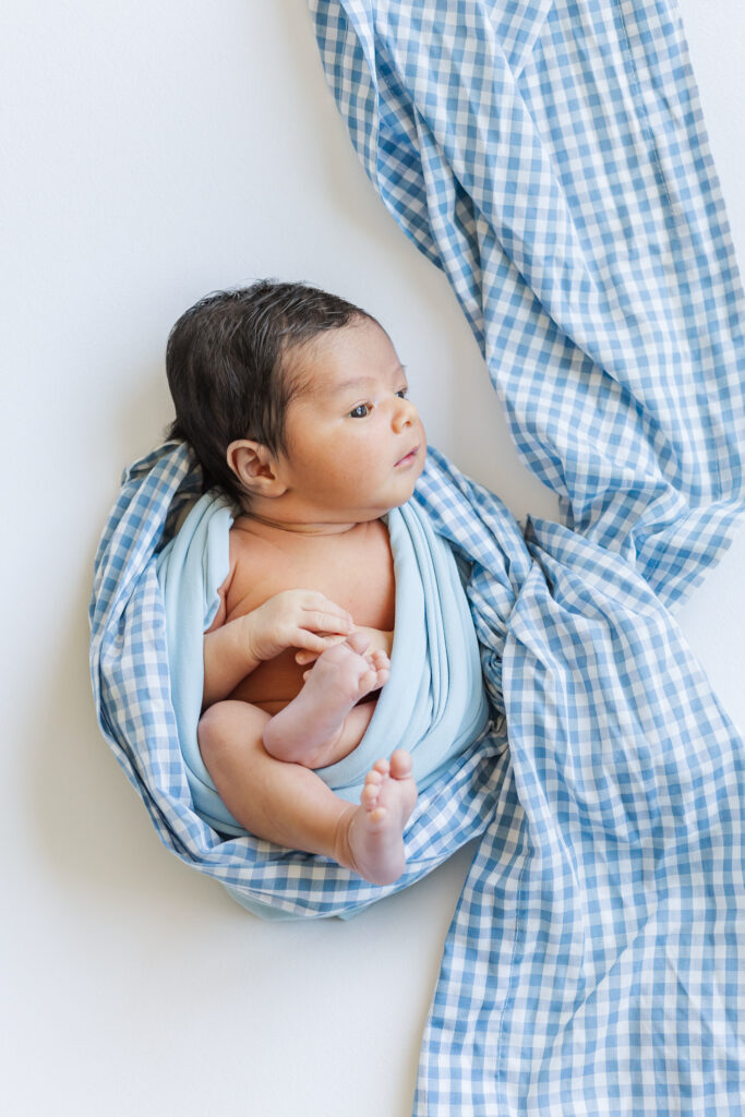 Baby boy wrapped in soft blue gingham blanket during professional in-home newborn photography in Trussville, Alabama.
