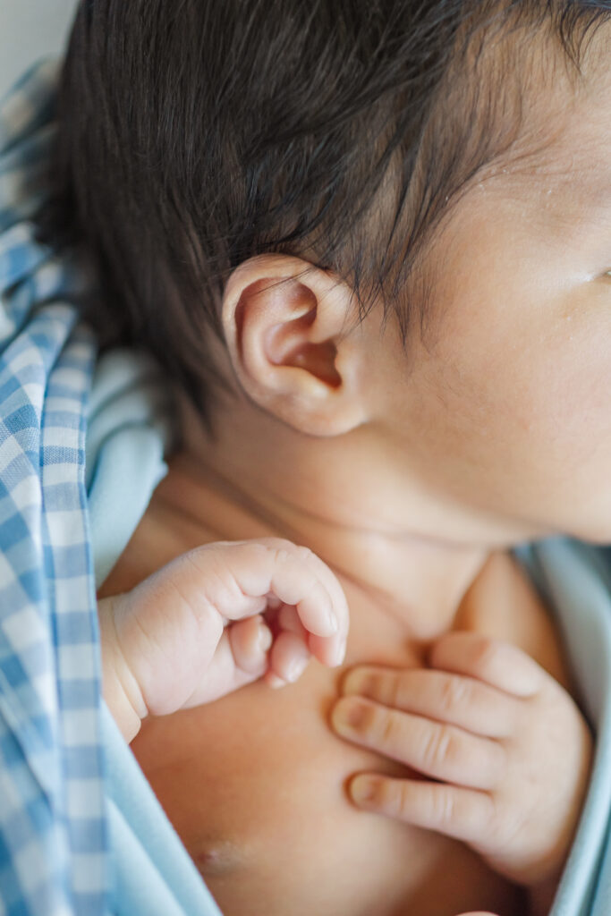 Macro detail of newborn baby’s tiny hand resting on chest beside ear during an in-home newborn session in Trussville, Alabama.
