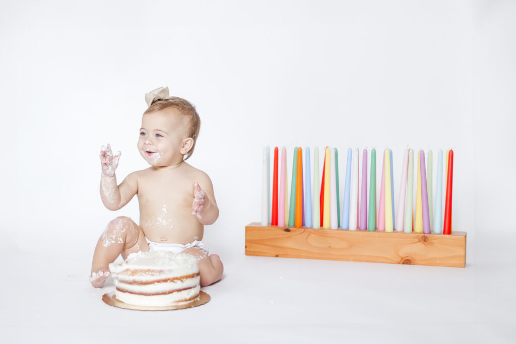 In-home one year milestone session in Birmingham, Alabama, featuring baby girl celebrating her first birthday with a simple cake smash on a white portable backdrop.