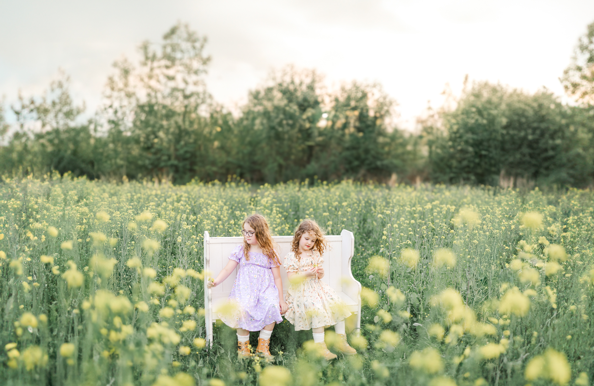 Heirloom spring mini session featuring two young girls seated on a white bench in a blooming wildflower field in Wilsonville, Alabama.