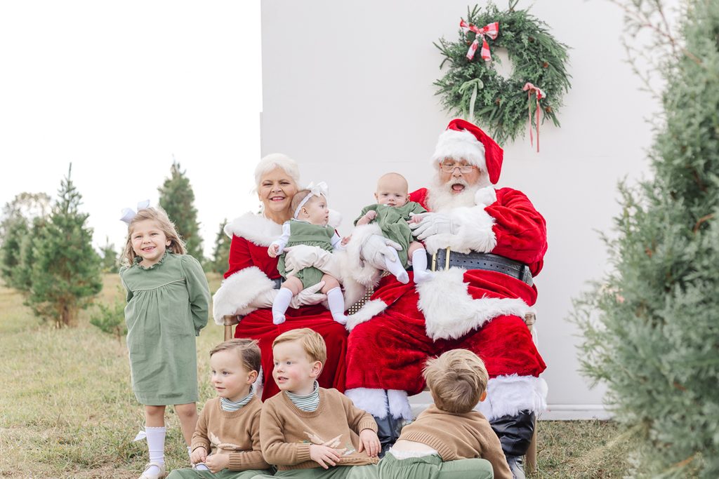 Group of children wearing coordinated green and brown holiday outfits with Santa and Mrs. Claus.