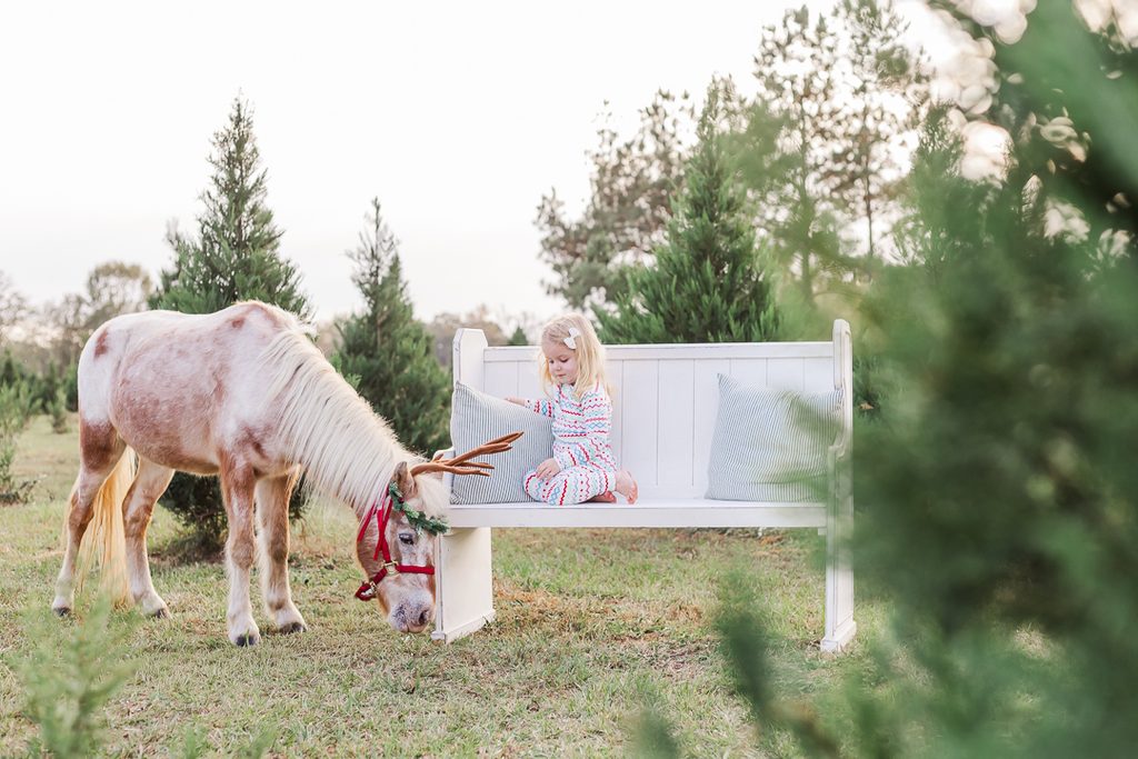 Child in festive pajamas enjoying a playful holiday moment beside Burt the Reindeer.