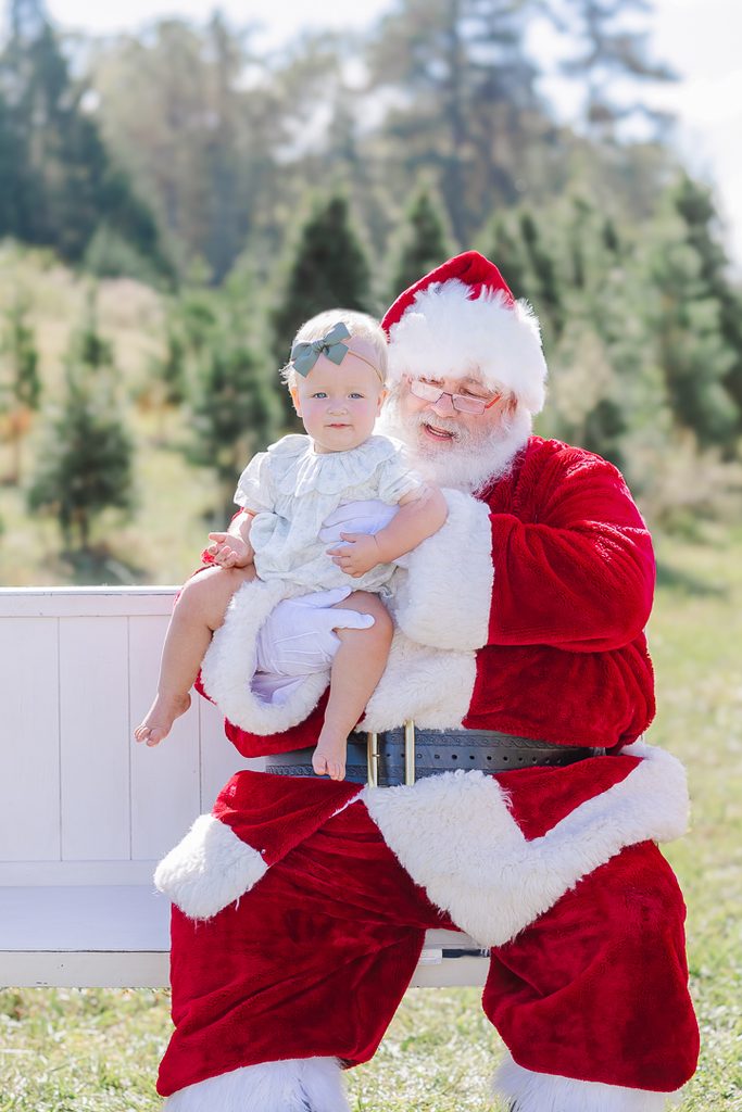 Young girl photographed in a festive Christmas outfit among evergreen trees.