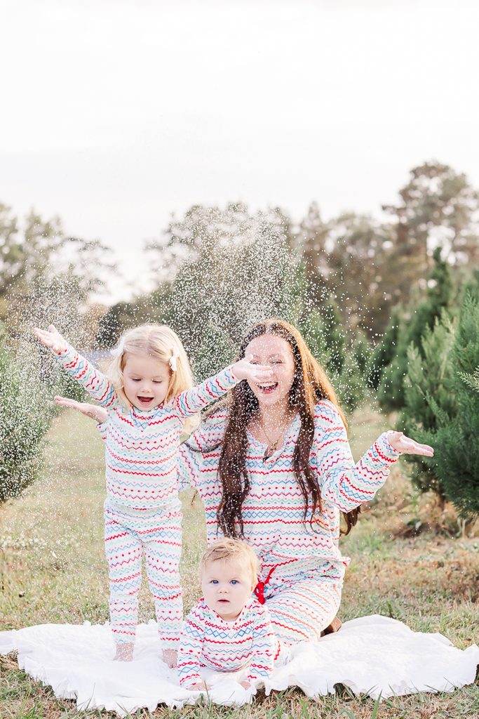 Mother and young children having fun together in matching Christmas pajamas outdoors.