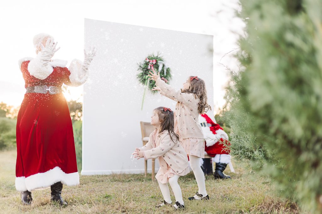 Family wearing soft neutral colors poses together among evergreen trees at a Christmas mini session.