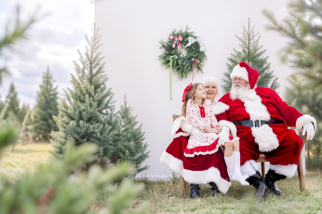 Family Christmas pajama photo with Santa, Mrs. Claus and a child in a festive patterned nightgown at the tree farm.