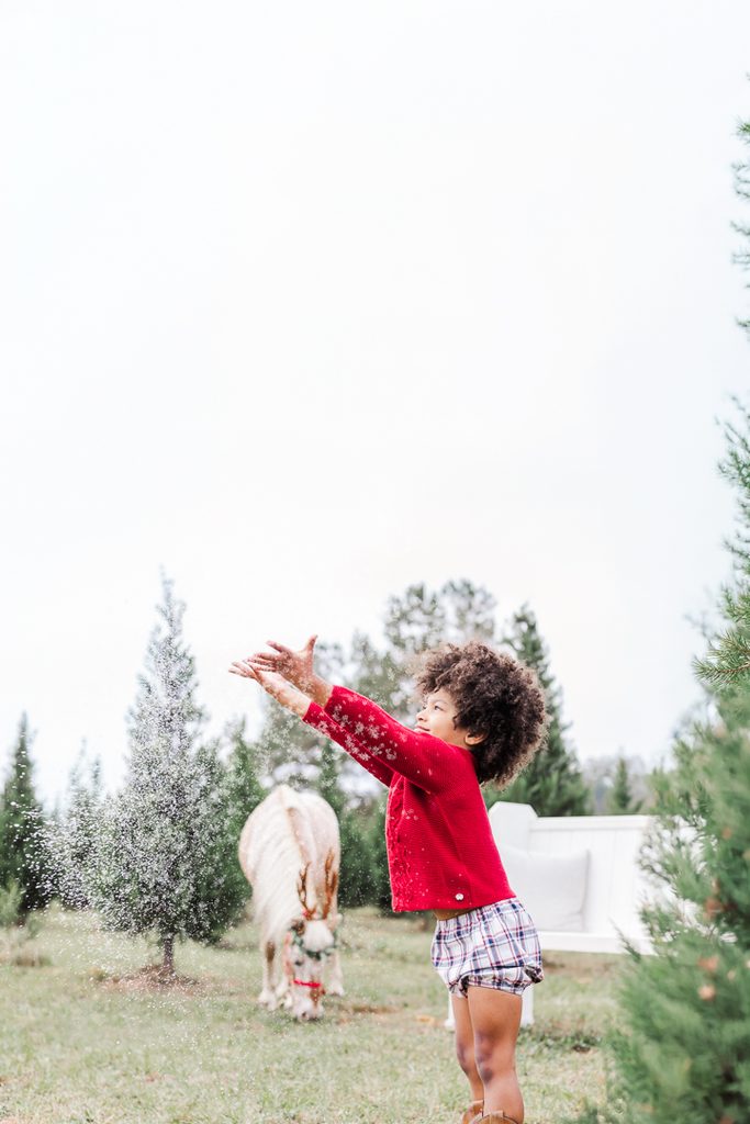 Child in a festive red Christmas outfit enjoying an outdoor holiday photography session.