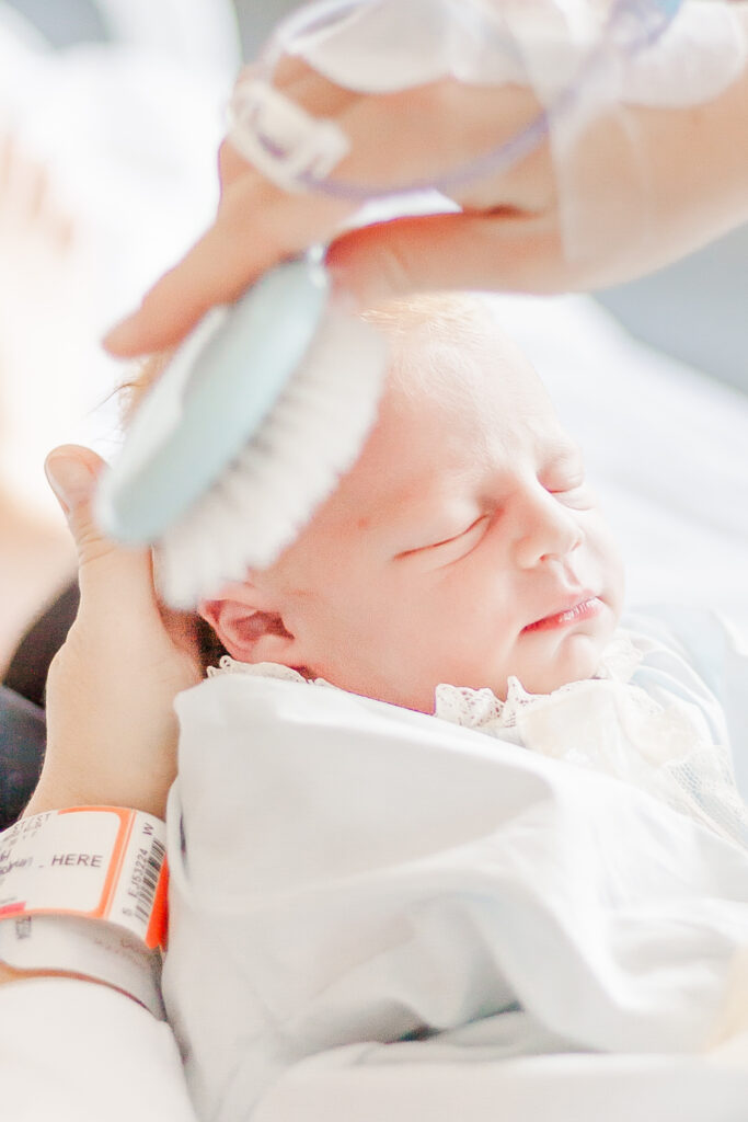 Mom brushing newborn's hair sitting in hospital bed in Birmingham, AL 