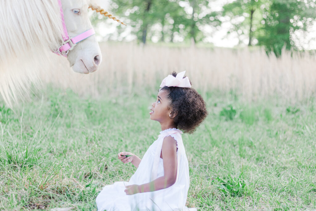 little girl sitting on the ground looking up at unicorn during mini session with 5U Photography 