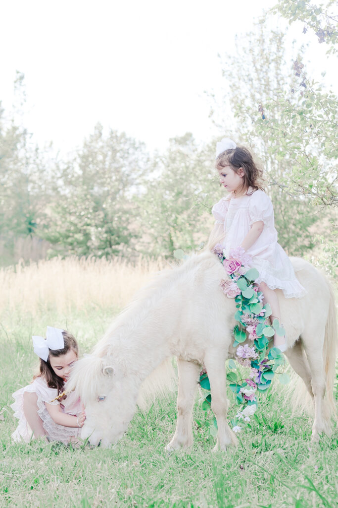 little girl sitting on white unicorn, while sister 