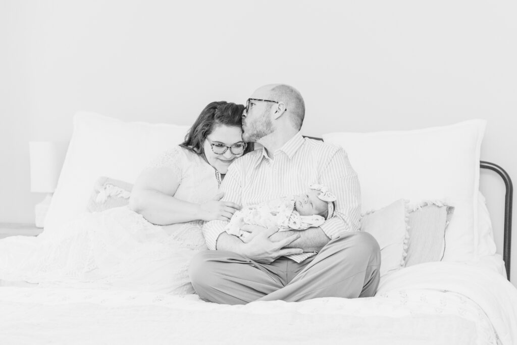 Mom and dad sitting on bed with newborn baby girl during in-home, lifestyle newborn session with 5U Photography in central Alabama