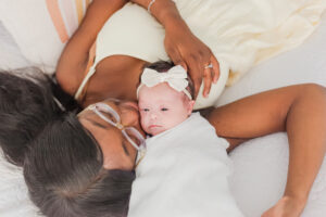 Mom laying with baby girl on bed during in-home, lifestyle newborn session