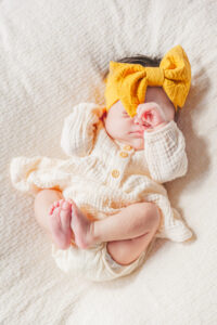 Baby girl laying on blanket with hand on face during in-home newborn session