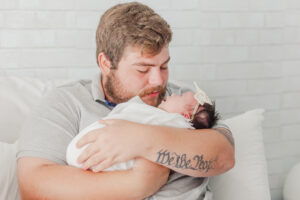 dad holding newborn baby girl looking down at baby during lifestyle newborn photography session