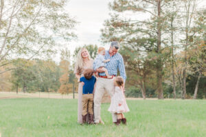 Family standing together in field looking at each other smiling during photo session with 5U Photography