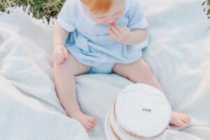 redheaded little boy sitting on blanket licking icing off his fingers from white cake 