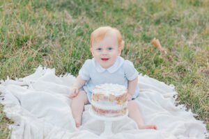 little boy sitting on blanket in front of smash cake smiling at the camera