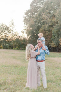 1 year old little boy sitting on dad's shoulders smiling down at mom smiling during 1 year milestone and smash cake session with 5U Photography