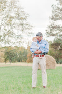 Dad holding son looking down at him smiling standing in field during 5U Photography session