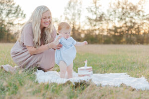 Mom holding redheaded little boy up while standing to look at white iced smash cake during smash cake session with 5U Photography