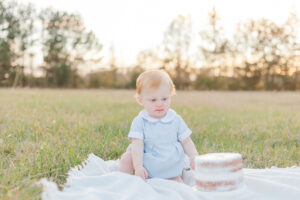 Little boy with red hair sitting on blanket looking down at smash cake during photo session with 5U Photography