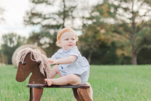 Little boy sitting on rocking horse looking away from camera smiling 