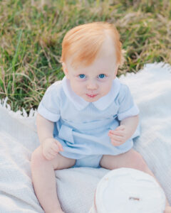 red headed little boy sitting on blanket looking up at camera in front of smash cake during milestone session with 5U Photography