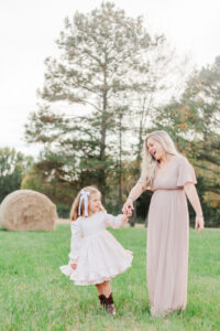 Little girt holding mom's hand in green field in front of hay bale during family photography session with 5U Photography 