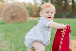 redheaded little boy pushing red wagon smiling at the camera during 1 year milestone and smash cake session with 5U Photography