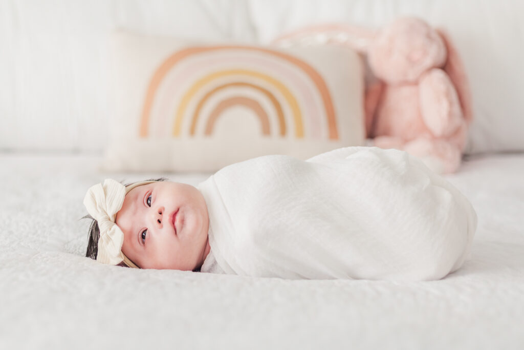 Baby girl swaddled with white blanket laying on bed